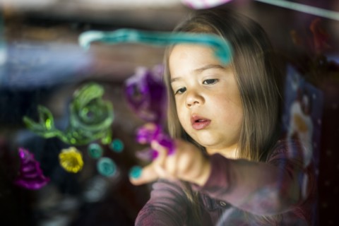 Mixed race girl finger painting on window