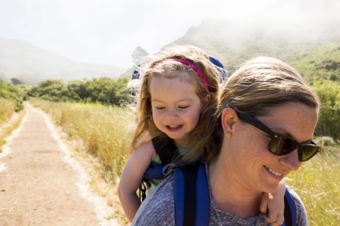 Caucasian mother carrying daughter while hiking