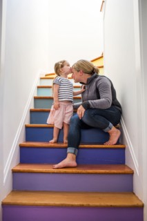 Caucasian girl kissing mother on forehead on multicolor staircase