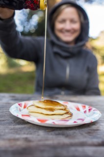 Smiling Caucasian woman pouring syrup on pancakes