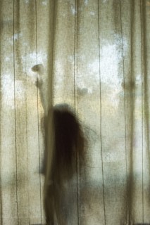 Silhouette of Caucasian girl touching heart-shape behind window curtain