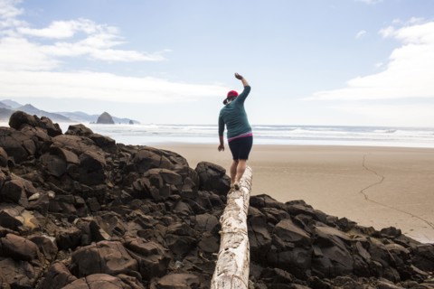 Caucasian woman balancing on log on rocks at beach