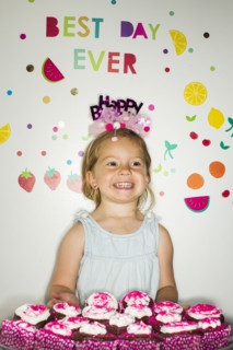 Caucasian girl holding tray of cupcakes for birthday