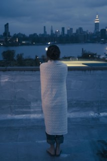 Caucasian woman wrapped in blanket admiring urban waterfront from rooftop