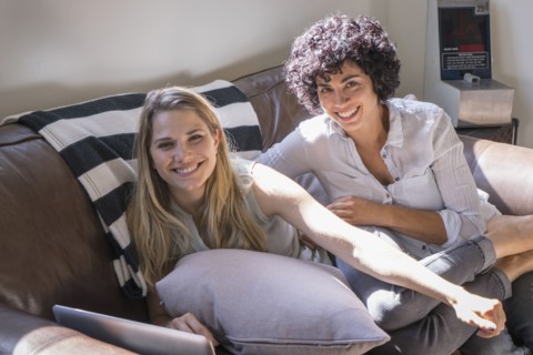 Caucasian lesbian couple smiling on sofa
