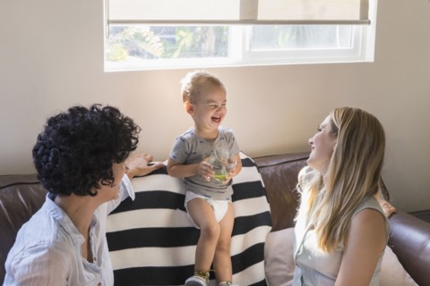 Caucasian lesbian mothers laughing with baby son on sofa