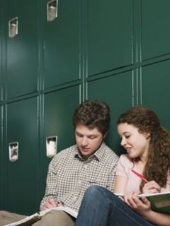 Students doing homework at locker in school hallway