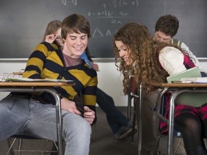 Students using cell phone at desk in classroom