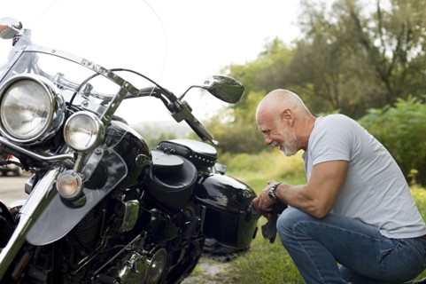 Older man repairing motorcycle in park
