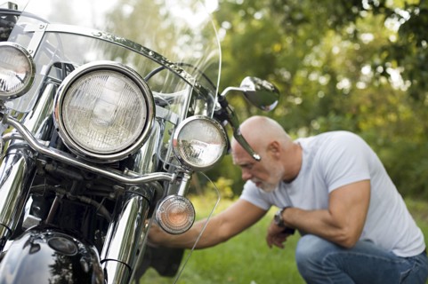 Older man repairing motorcycle in park