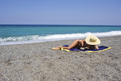 Woman sunbathing and reading on beach