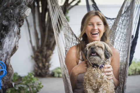 Caucasian woman in hammock holding dog and laughing