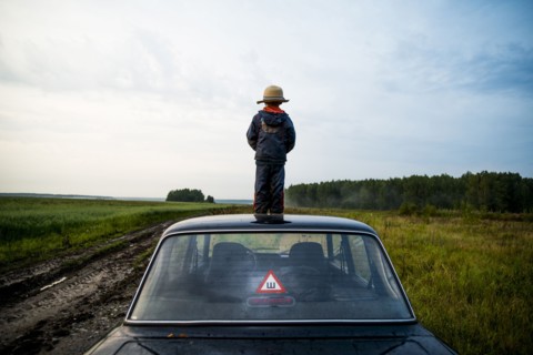 Caucasian boy standing on car roof in rural field