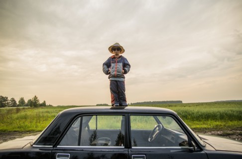 Caucasian boy standing on car roof in rural field