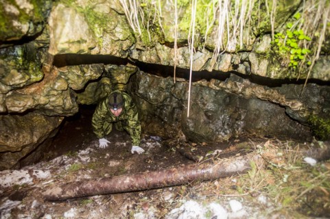 Caucasian man climbing out of rock formation cave