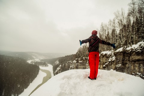 Caucasian hiker standing with arms outstretched on snowy hilltop