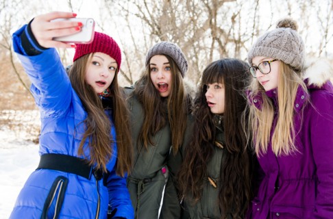 Caucasian girls taking cell phone photograph in snowy field