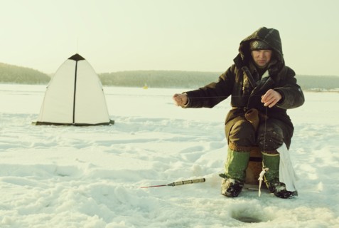 Caucasian man ice fishing on remote lake