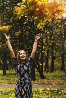 Caucasian woman tossing autumn leaves in park
