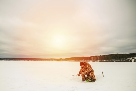 Man ice fishing in frozen lake