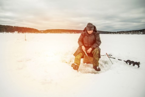 Man ice fishing in frozen lake