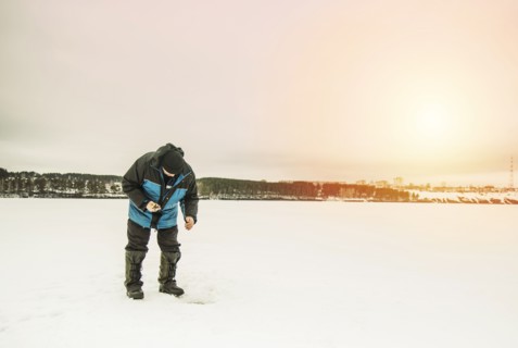 Man ice fishing in frozen lake