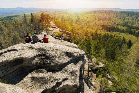 Caucasian friends sitting on mountain rock admiring scenic view