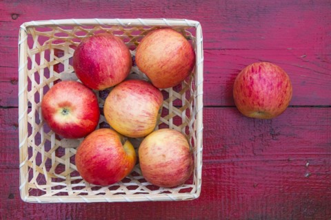 Close up of basket of red apples on red wooden table