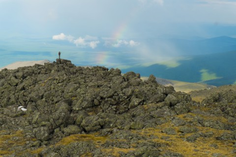 Man standing on rock formation looking at rainbow