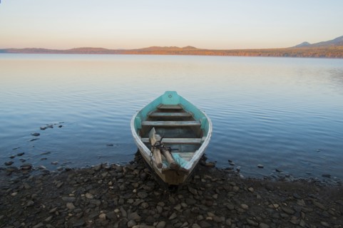 Empty rowboat on rocky shore of lake at sunset