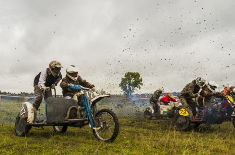 Caucasian racers on motorcycles with side cars spraying dirt
