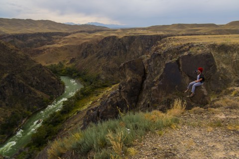 Caucasian woman sitting on mountain rocks photographing river