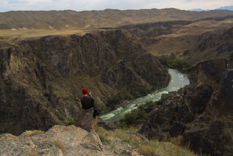 Caucasian woman sitting on mountain rocks photographing river