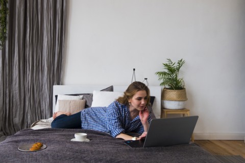Caucasian woman laying on bed using laptop