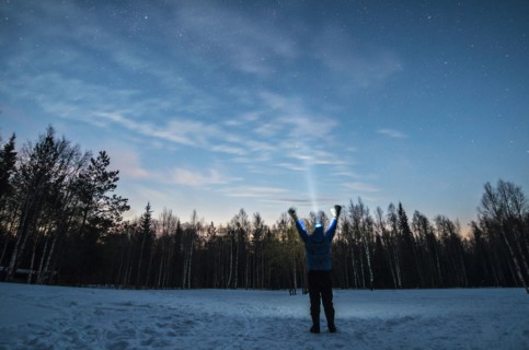 Caucasian man wearing headlamp with arms raised in winter