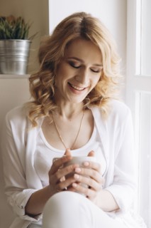 Middle Eastern woman sitting in window sill drinking coffee