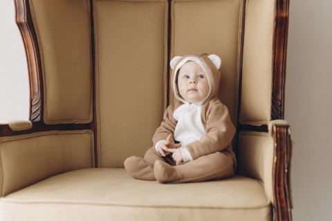 Caucasian baby boy sitting in armchair wearing bear costume
