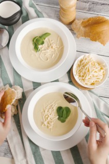 Hands of woman eating bowl of cheese soup