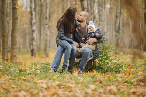 Middle Eastern couple sitting on tree stump with baby son in autumn