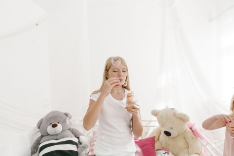 Middle Eastern girl blowing bubbles in bedroom