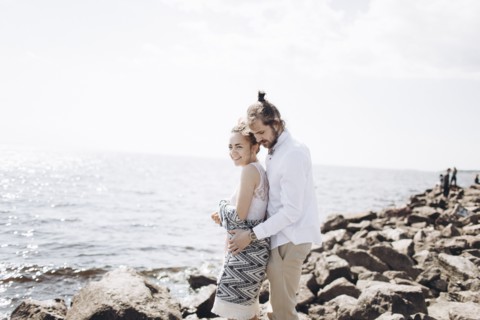 Middle Eastern couple hugging on rocks near ocean