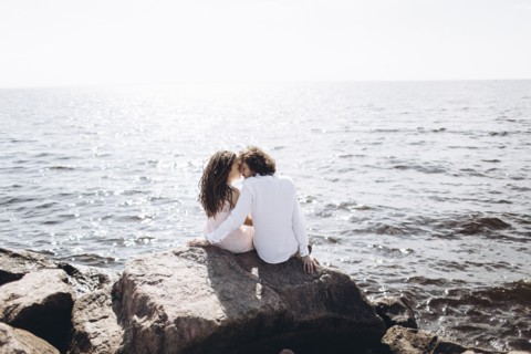 Middle Eastern couple sitting on rocks near ocean