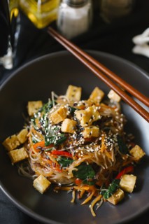 Chopsticks on bowl with noodles and tofu