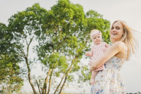 Mother carrying baby daughter near tree