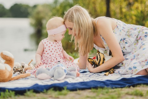 Mother and daughter playing with stuffed animals on blanket near lake
