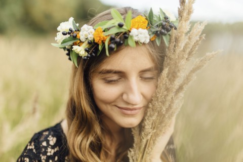 Middle Eastern woman wearing flower crown holding wheat to face