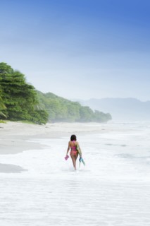 Hispanic woman carrying fins on beach