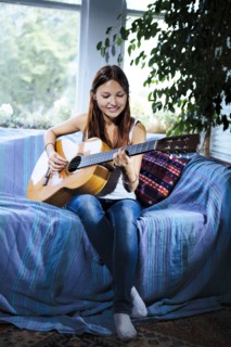 Mixed race woman playing guitar on sofa