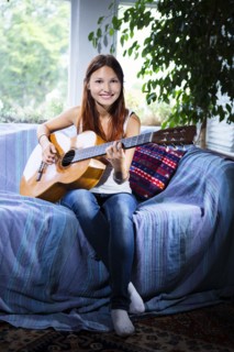 Mixed race woman playing guitar on sofa
