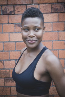 Black athlete smiling near brick wall